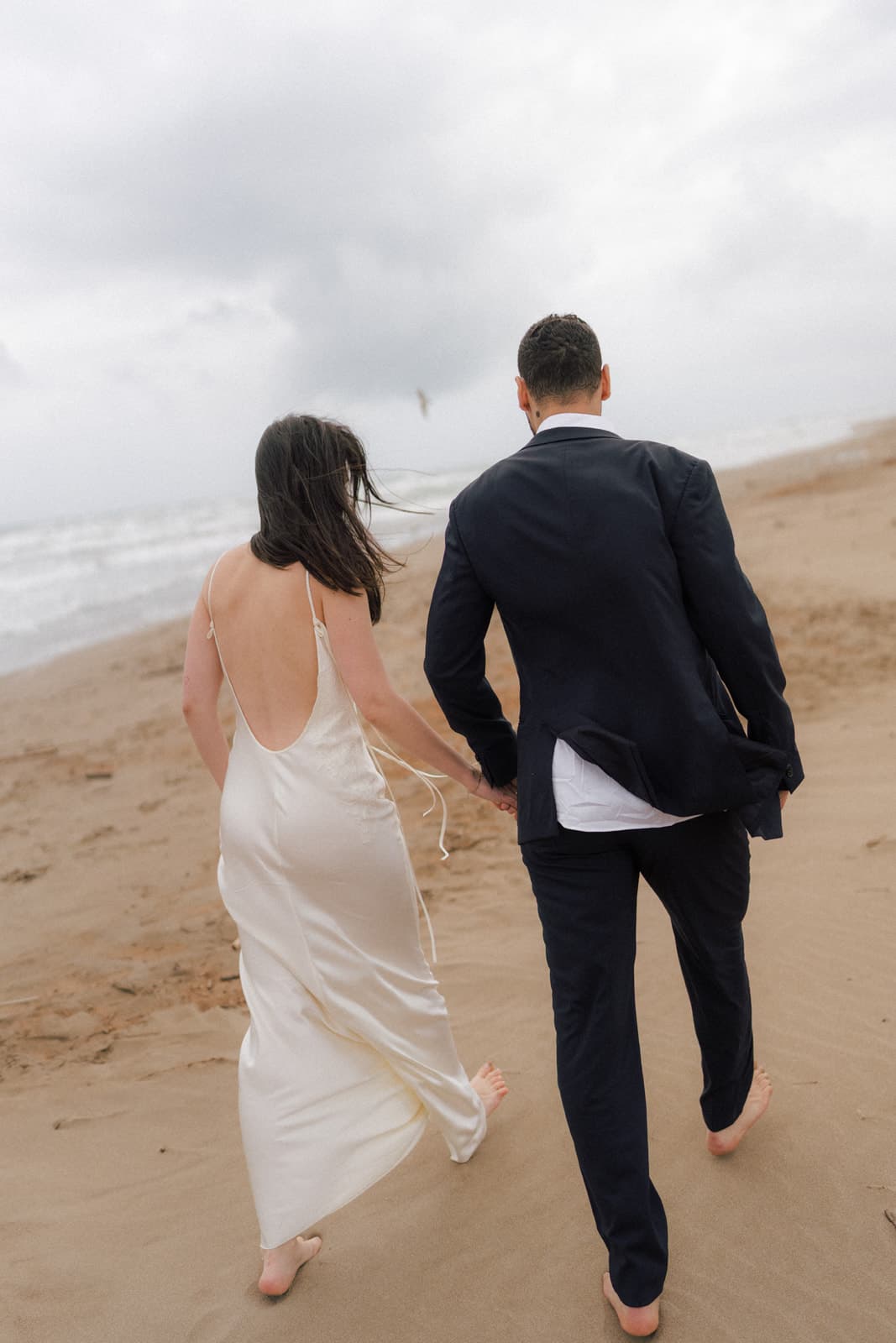 Couple de mariés marchant sur la plage, main dans la main